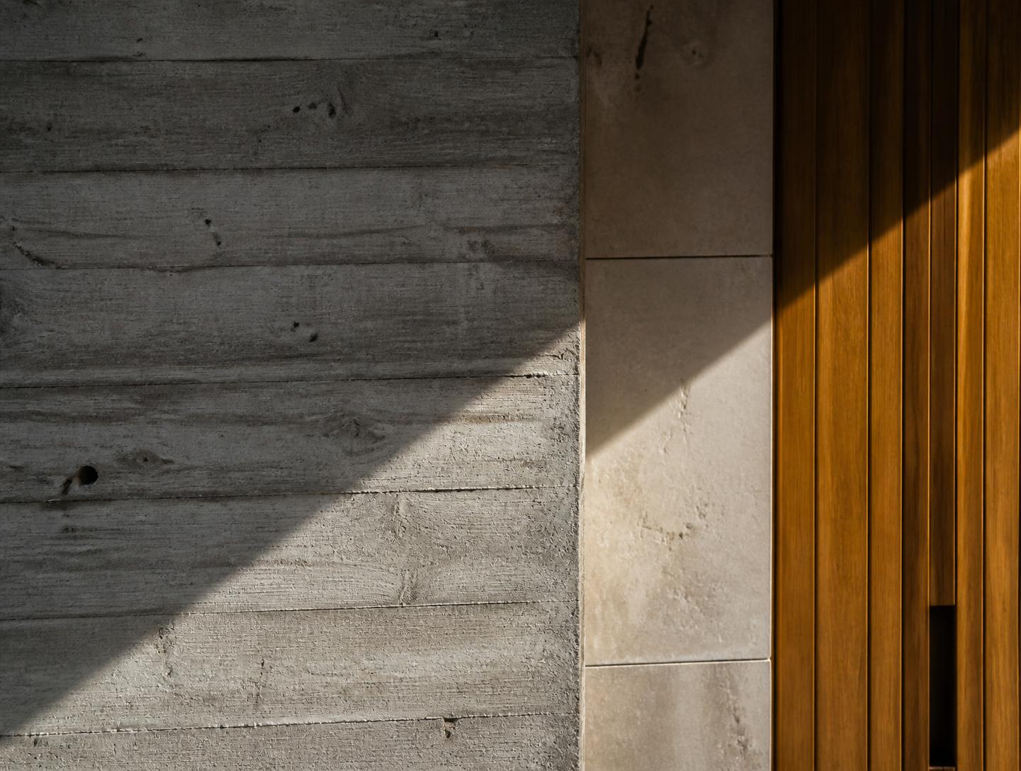 Detalhe de betão moldado, pedra lioz e madeira sob luz rasante